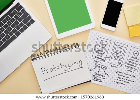 top view of gadgets near website design template and notebook with prototyping lettering on yellow background