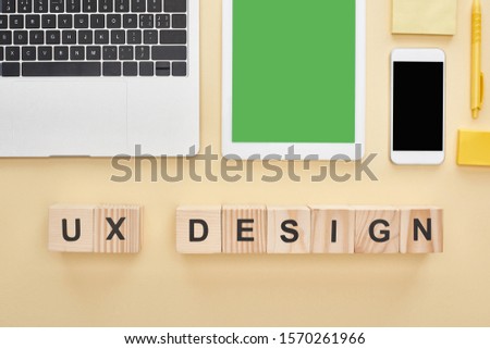 flat lay with gadgets and wooden blocks with ux design lettering on yellow background