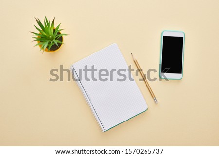 top view of green plant, blank notebook near pencil and smartphone on beige background