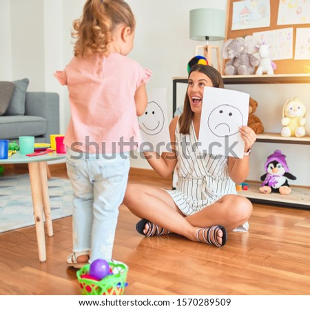 Beautiful psycologist and blond toddler girl sitting on the floor doing therapy using emoji emotions at consulting room