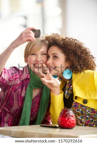 Two teenage girls taking a photograph of themselves in a café