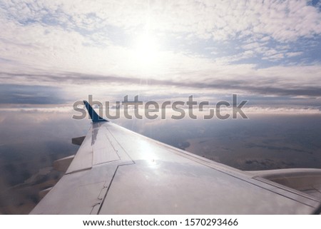 Wing of the plane on the background of a beautiful blue sky with snow-white lush clouds during flight.