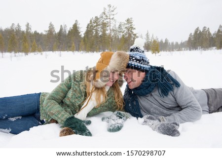 A young couple dressed in warm clothes laying in the snow