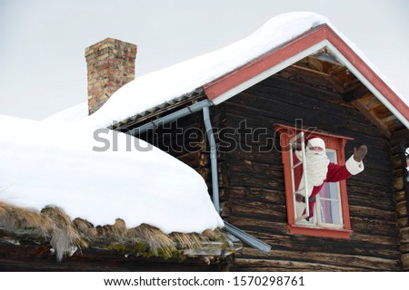 Santa Claus waving from the window of his log cabin