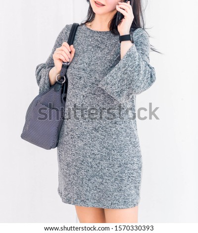 Photo of A woman in a gray dress and a large dark bag dressed over her shoulder is talking on the phone.