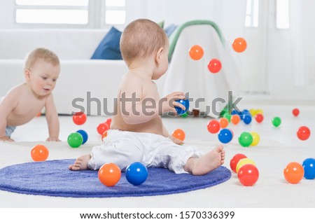Two young children sitting on the floor playing with balls