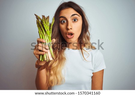 Young beautiful woman eating asparagus over grey isolated background scared in shock with a surprise face, afraid and excited with fear expression