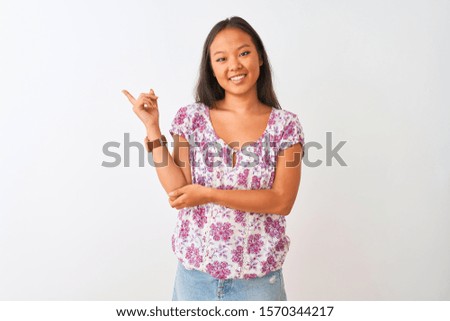 Young chinese woman wearing casual floral t-shirt standing over isolated white background with a big smile on face, pointing with hand and finger to the side looking at the camera.