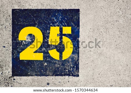 Number 25, twenty-five, blue and yellow stencil painted on gray background.