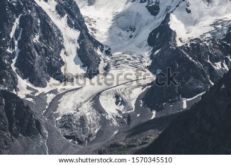 Atmospheric minimalist textured alpine landscape of snowy rocky mountain with glacier tongue. Background of snowbound mountainside. Meltwater from ice on steep slope. Majestic scenery on high altitude