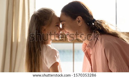 Cheerful family young mother and cute small daughter bonding touching noses in sunny room at home, happy parent mum cuddling with little preschool child girl enjoy sweet tender moment of love care