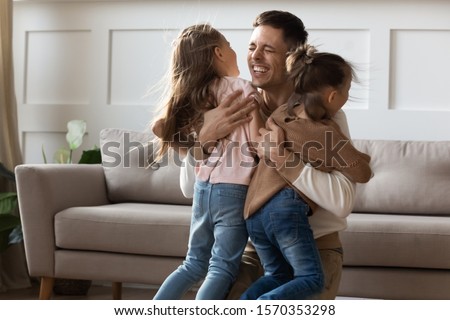 Cheerful happy young adult dad embracing cute kids daughters cuddling at home celebrate reunion, overjoyed single father hugging little children girls bonding enjoy time together, custody concept Royalty-Free Stock Photo #1570353298
