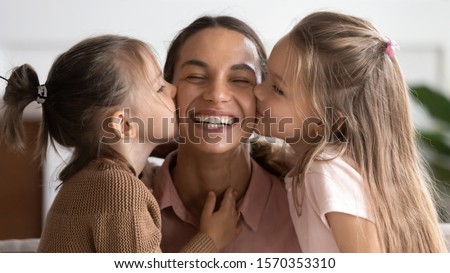 Two cute adorable little daughters kissing happy mum on cheeks congratulate mom with mothers day, cheerful mommy smiling face and small children girls bonding cuddling together express love and care