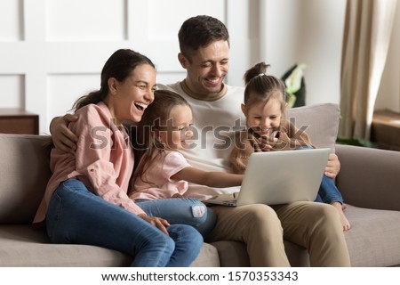 Happy positive family young parents couple and cute little children daughters laugh using laptop computer relax on sofa enjoy watching funny videos bonding look at notebook screen sit on sofa at home