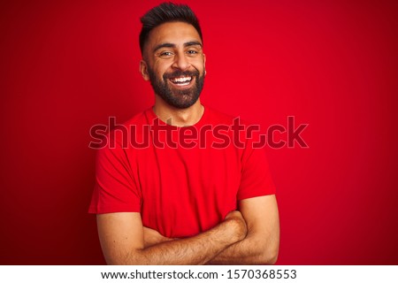 Young handsome indian man wearing t-shirt over isolated red background happy face smiling with crossed arms looking at the camera. Positive person.