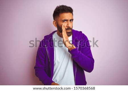 Young indian man wearing purple sweatshirt standing over isolated pink background hand on mouth telling secret rumor, whispering malicious talk conversation
