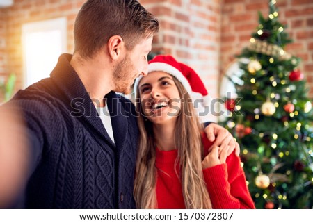 Young beautiful couple smiling happy and confident. Standing make selfie by camera around christmas tree at home