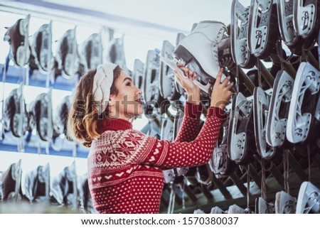 A beautiful girl wearing a warm sweater choosing a pair of skates