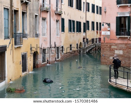 Female photographer taking pictures of the narrow alley over the canal Venice, November 2019