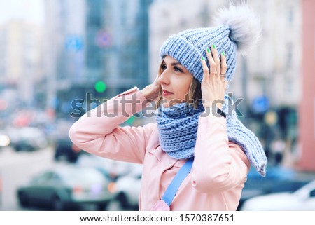 Outdoor close up portrait of young beautiful happy smiling girl wearing knitted beanie hat, and gloves. Model posing in street. Winter holidays concept. Toned. 