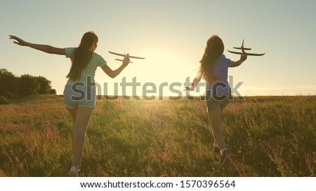Happy childhood concept. Dreams of flying. Two girls play with toy plane at sunset. Children on background of sun with an airplane in hand. Silhouette of children playing on plane