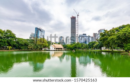 Bangkok cityscape view from Lumpini park in city center. Panoramic photo of skyscrapers and futuristic buildings from metal and glass. View from the small lake in Lumpini park. Fresh green plants.