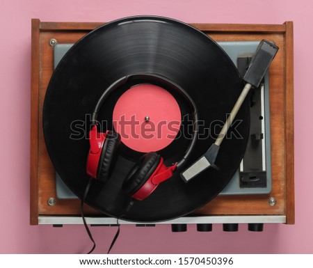 Old-fashioned vinyl player, headphones on pink pastel background. Media 70s.