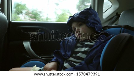 
Passenger child in the backseat of a car wearing raincoat during rainy day