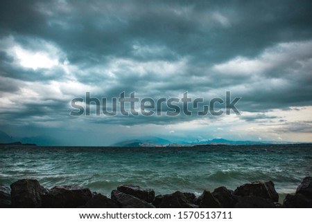 Panoramic view of the coast of Garda lake in Desenzano del Garda, Province Brescia, Lombardy, Italy. A storm on a lake with big green waves, rain and heavy clouds in the grey sky. 