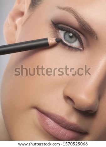 Close-up portrait of young woman applying eyeliner, studio shot Royalty-Free Stock Photo #1570525066
