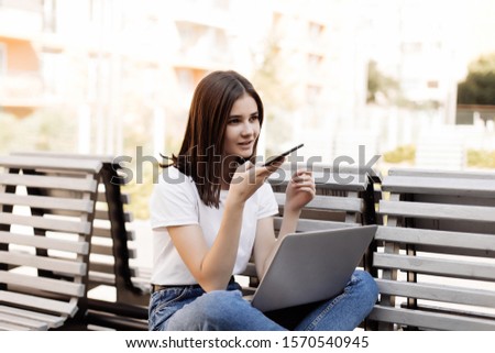 woman sitting on bench in park talking on cell phone and using laptop.