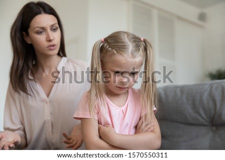 Angry young adult mom scold stubborn fussy upset little kid daughter sulking sit on sofa ignore parent, single mother shout at unhappy preschool difficult child girl punish for bad behavior at home Royalty-Free Stock Photo #1570550311