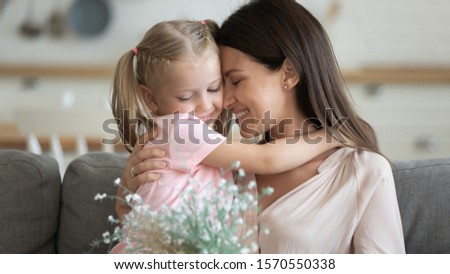Happy family grateful attractive young mum holding spring flowers embracing sweet adorable little child daughter at home, cute small kid girl hugging mom presenting bouquet on mothers day concept