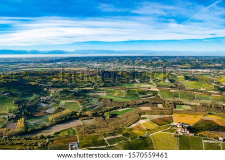 Spectacular autumn aerial view of the 
Piedmontese Langhe, Unesco heritage site, with its famous vineyards, producers of fine Barolo. in the background the chain of the Alps wine. 