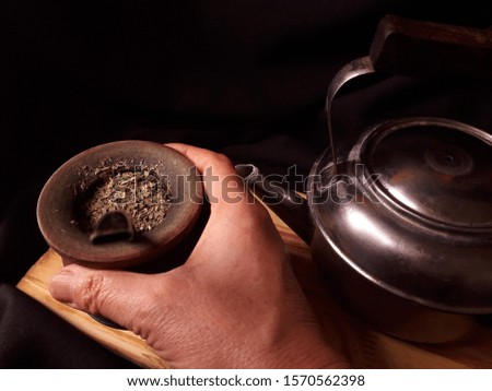 Woman hand holding a yerba mate tea cup. Black backgriund. Dark food photography. Space copy.