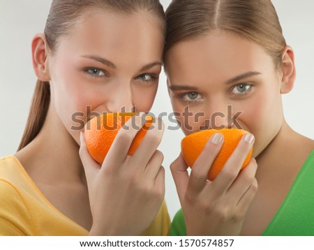 Portrait of two young women eating oranges, studio shot