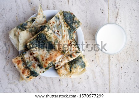  Gozleme with cottage cheese and spinach - delicious fresh Turkish pastries made by hand on a white plate with ayran in a glass on a concrete light background. Traditional Turkish Tortilla            