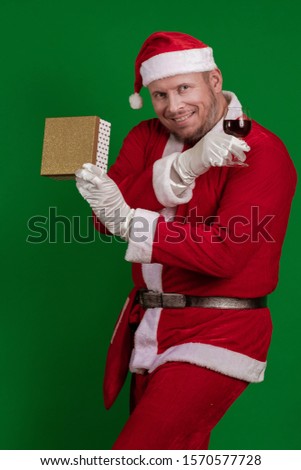 Santa Claus holds one gift box and a glass of wine in his hands and poses on a green chrome background