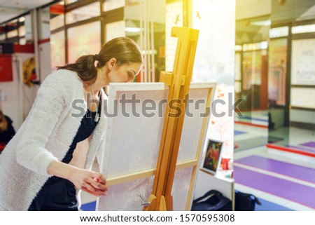 Young beautiful female girl woman artist painter painting standing in front of the canvas easel at home or studio paint adjusting frame