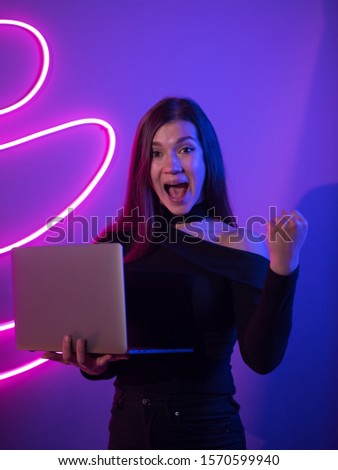 Woman looks in surprise at the laptop. Neon light background