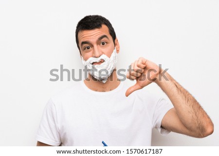 Man shaving his beard over isolated white background showing thumb down