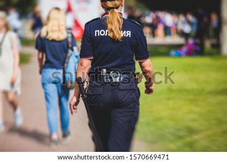 Russian female police squad formation back view with "Police" emblem on uniform maintain public order after football game with football fans crowd in the background
