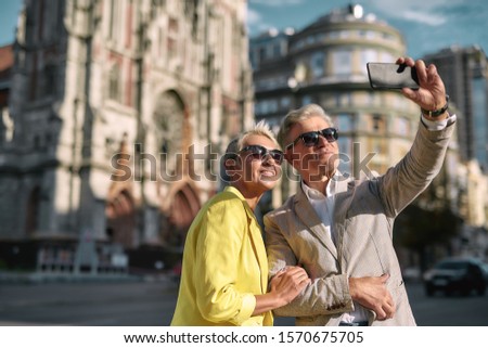 Happy moments. Beautiful mature caucasian couple in sunglasses taking selfie by mobile phone while spending time together outdoors