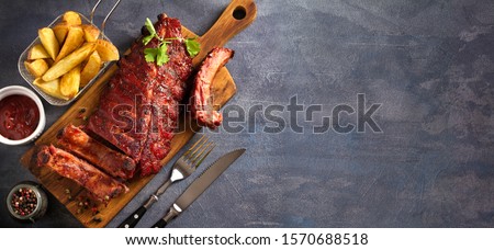 Pork loin ribs served on chopping board and potato wedges. View from above, top. Copy space Royalty-Free Stock Photo #1570688518