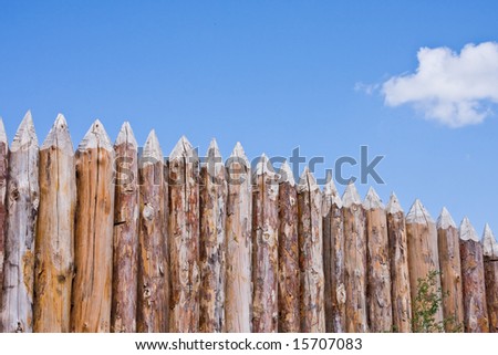 Fence from the pointed logs on a background of the blue sky
