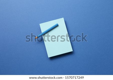 Blue memo note pad and blue colored pencil on blue background