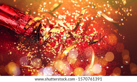 Bottle of red champagne with gold glitter, sparkles, confetti on red background, top view. New year background. Selected focus.