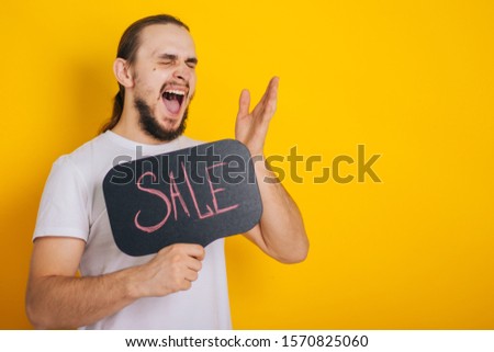A guy in a white T-shirt on a yellow background with a sign saying Sale