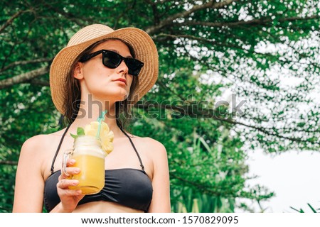 Relaxed woman in bikini enjoying tropical resort, drinking pineapple cocktail