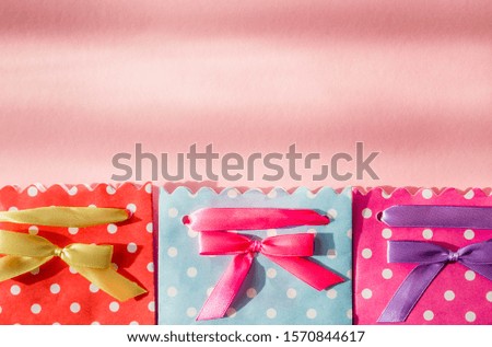 Photo of Three gift bags - blue, pink and red polka dots, with a bow photographed on a pink background from above. The shadow from the sun is falling